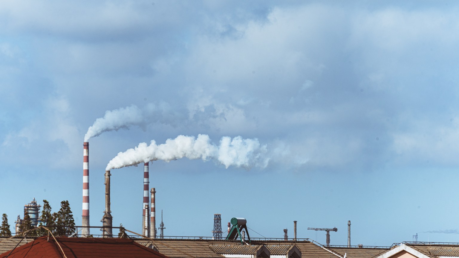 Factory chimneys emitting smoke over rooftops on a clear day, illustrating urban pollution.