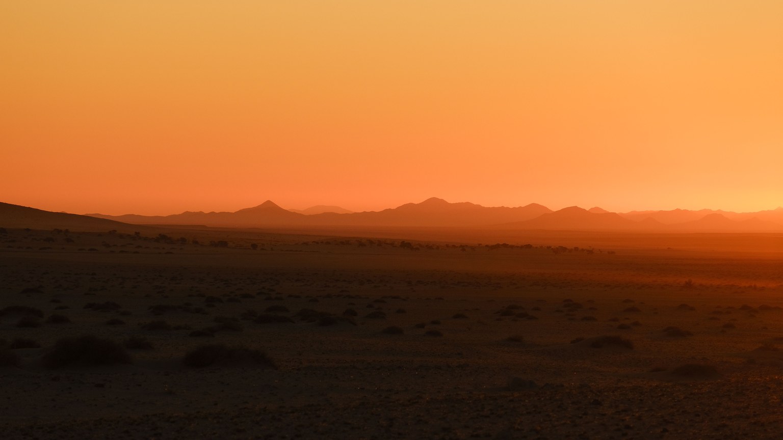 A breathtaking view of a desert landscape with a vibrant sunset illuminating the horizon.