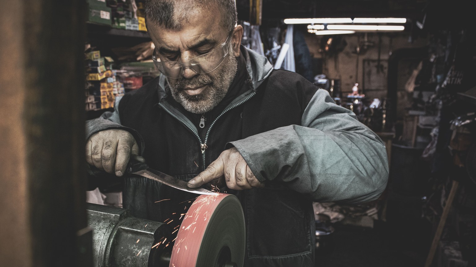 Skilled craftsman sharpens a blade on a grinding wheel, creating sparks in a workshop.