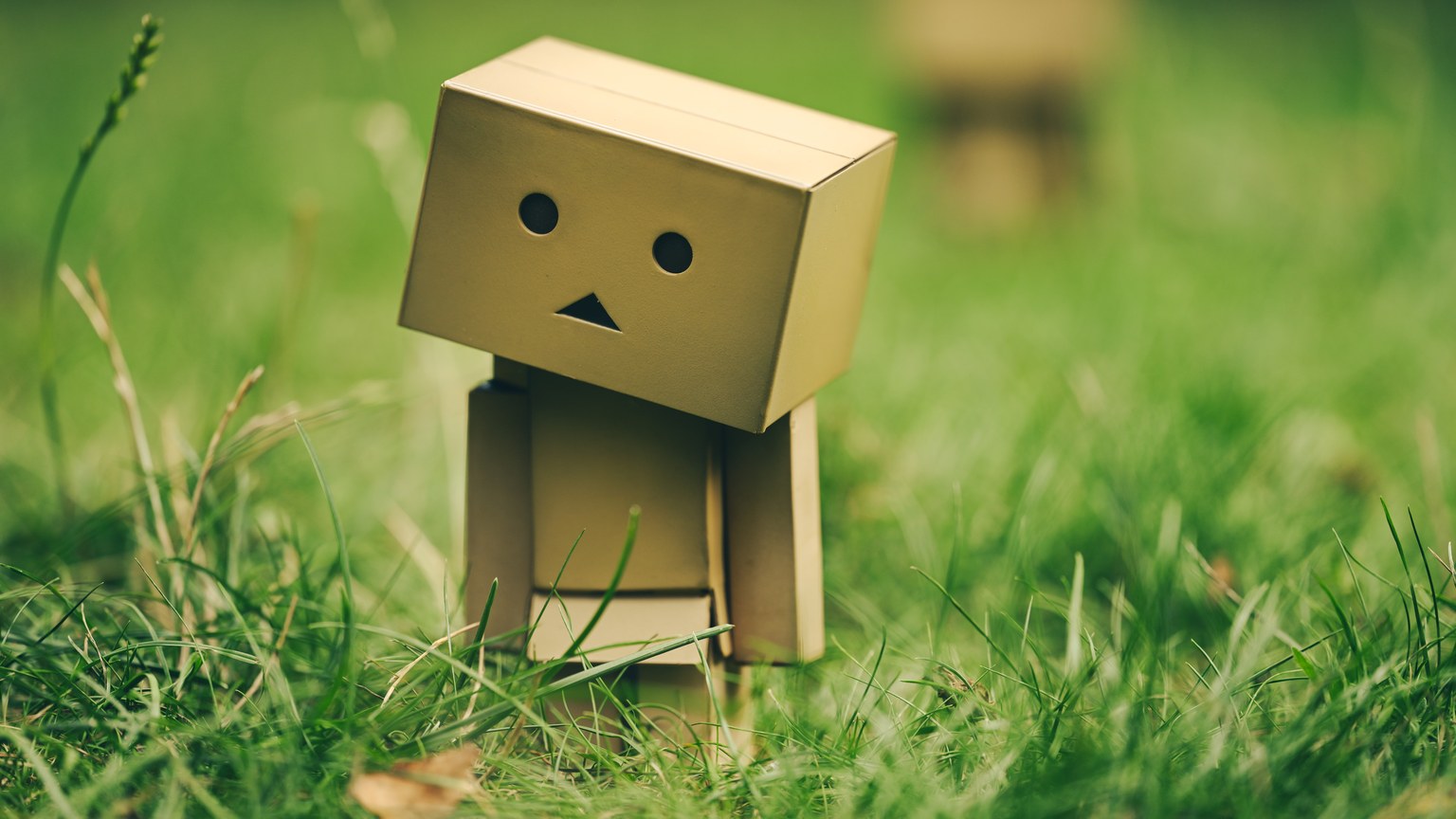A cardboard robot figurine standing amid lush green grass outdoors during the day.