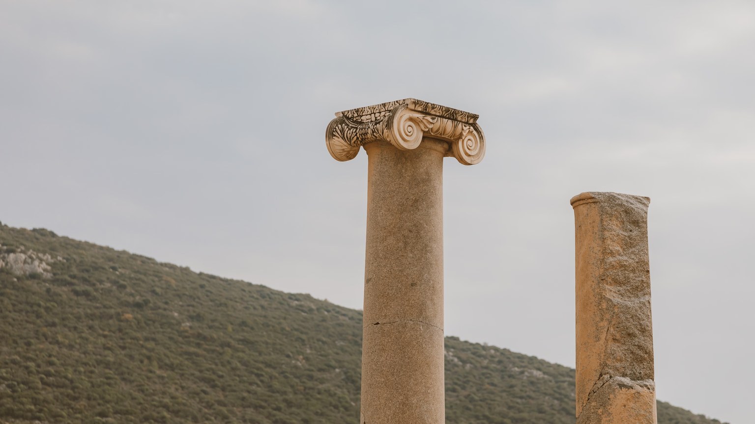 Two ancient columns stand majestically against a serene hillside backdrop.