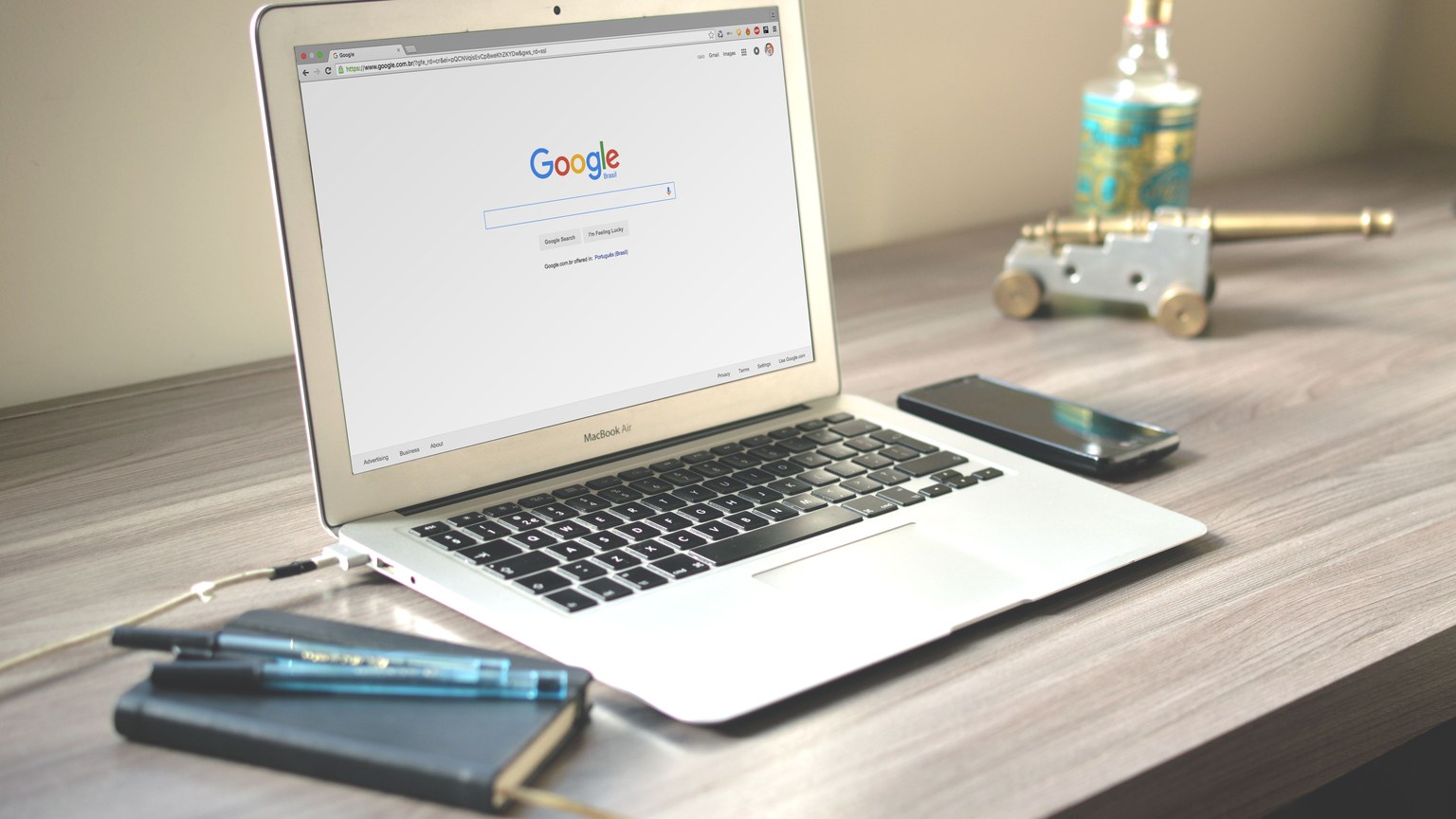 A neat workspace featuring a laptop displaying Google search, a smartphone, and a notebook on a wooden desk.