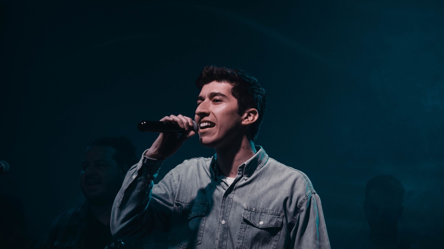 Young male singer performing passionately with microphone on stage. Captured in Mendoza, Argentina.