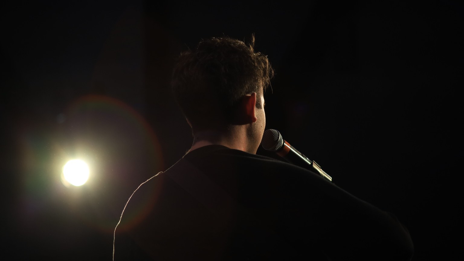 Silhouette of a singer on stage with a microphone, spotlight in the black background.