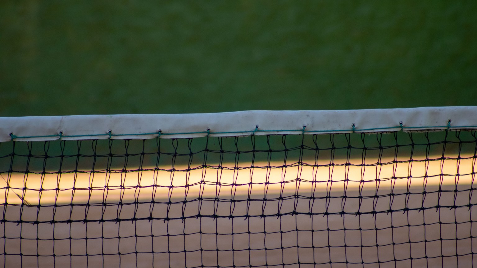 A detailed view of a tennis court net at dusk with a green court background, showcasing sports equipment.