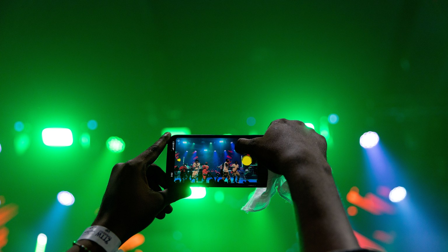 A vibrant live concert scene captured through a smartphone under green stage lighting.
