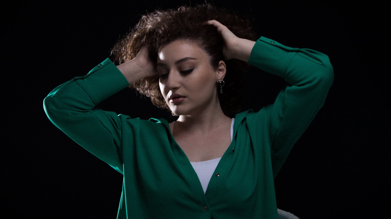 Studio portrait of a brunette woman in green shirt posing gracefully against a dark background.