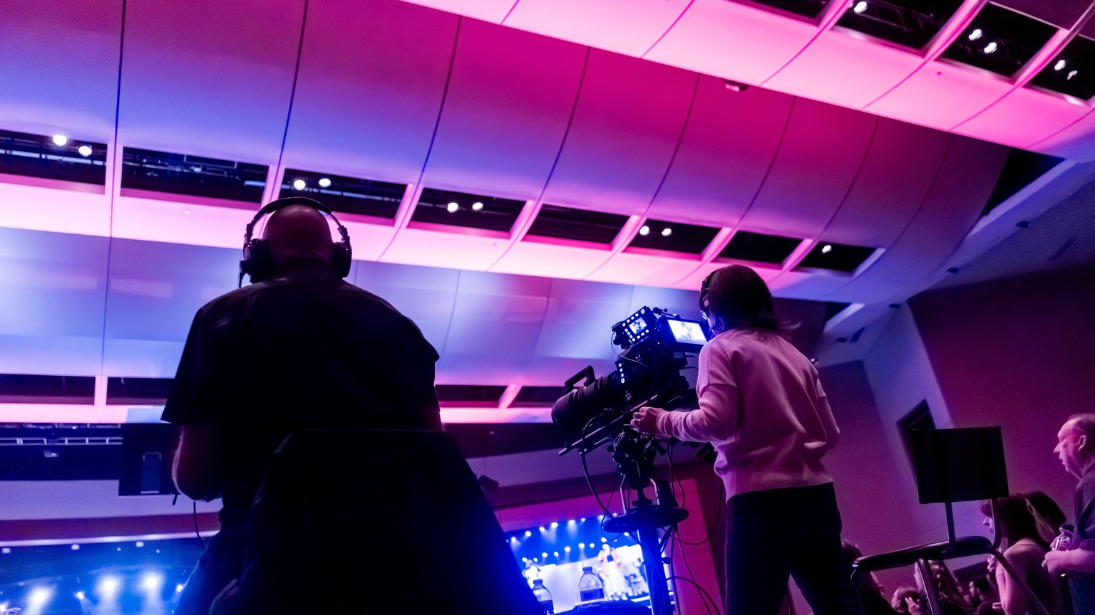 Professional camera crew filming a live event indoors, capturing vibrant stage lighting.