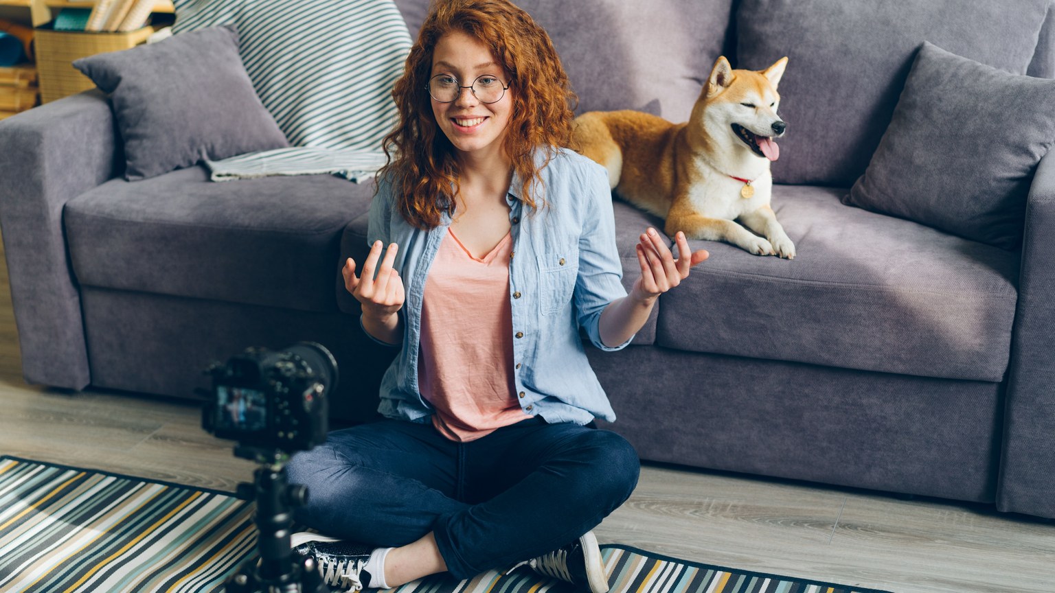 Redhead woman recording a video at home with her Shiba Inu dog on the couch.
