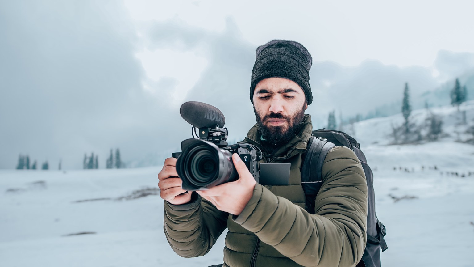 A bearded man with a camera captures winter scenery in Gulmarg, showcasing snow and travel photography.