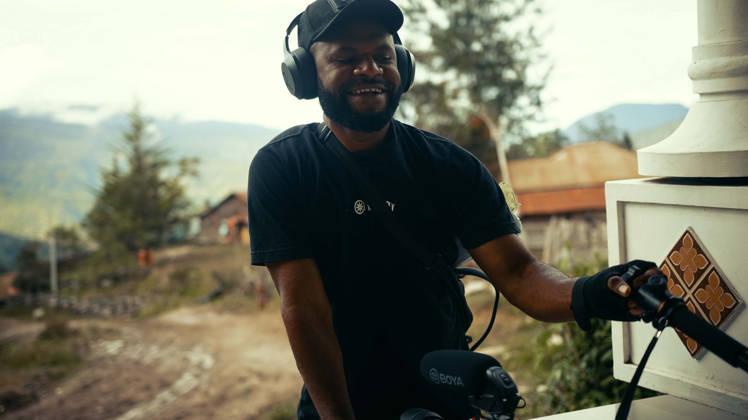 A videographer works with equipment outdoors in a beautiful mountain setting.