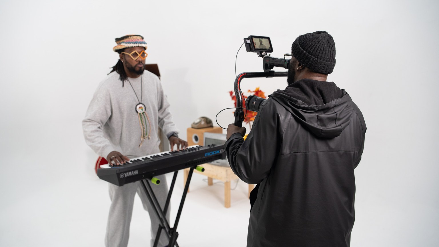 A musician plays a keyboard while a videographer films in a bright studio.