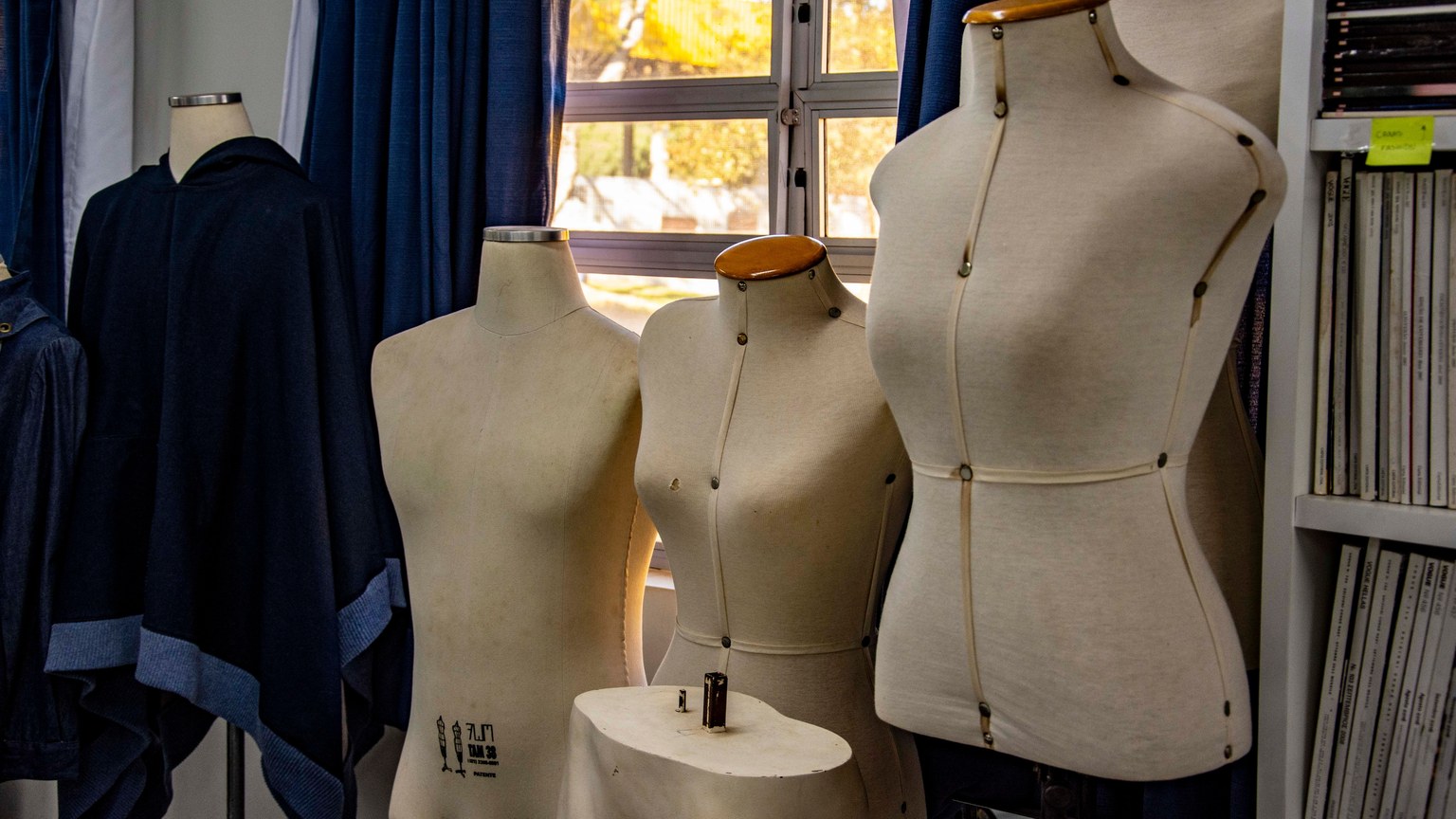 A glimpse into a fashion design studio featuring dress forms against a window backdrop.