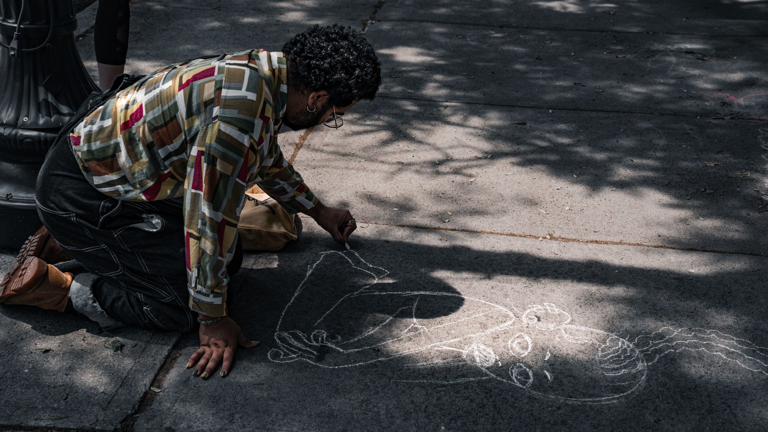 A street artist drawing chalk art on a sunlit urban sidewalk, showcasing creativity.