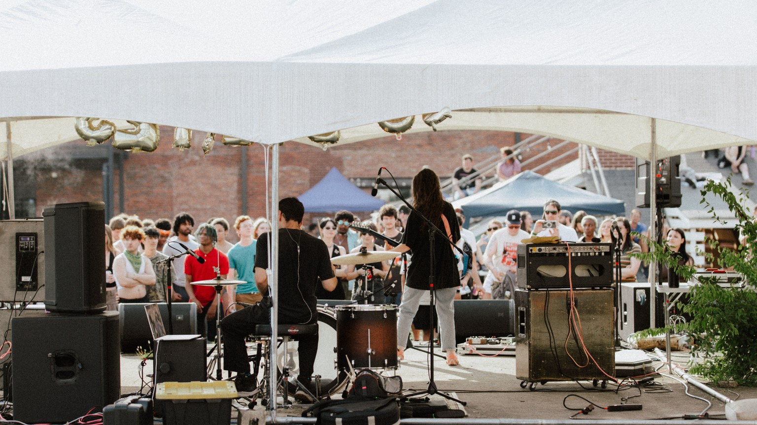 A lively outdoor band performance with an energetic crowd enjoying live music under a tent.