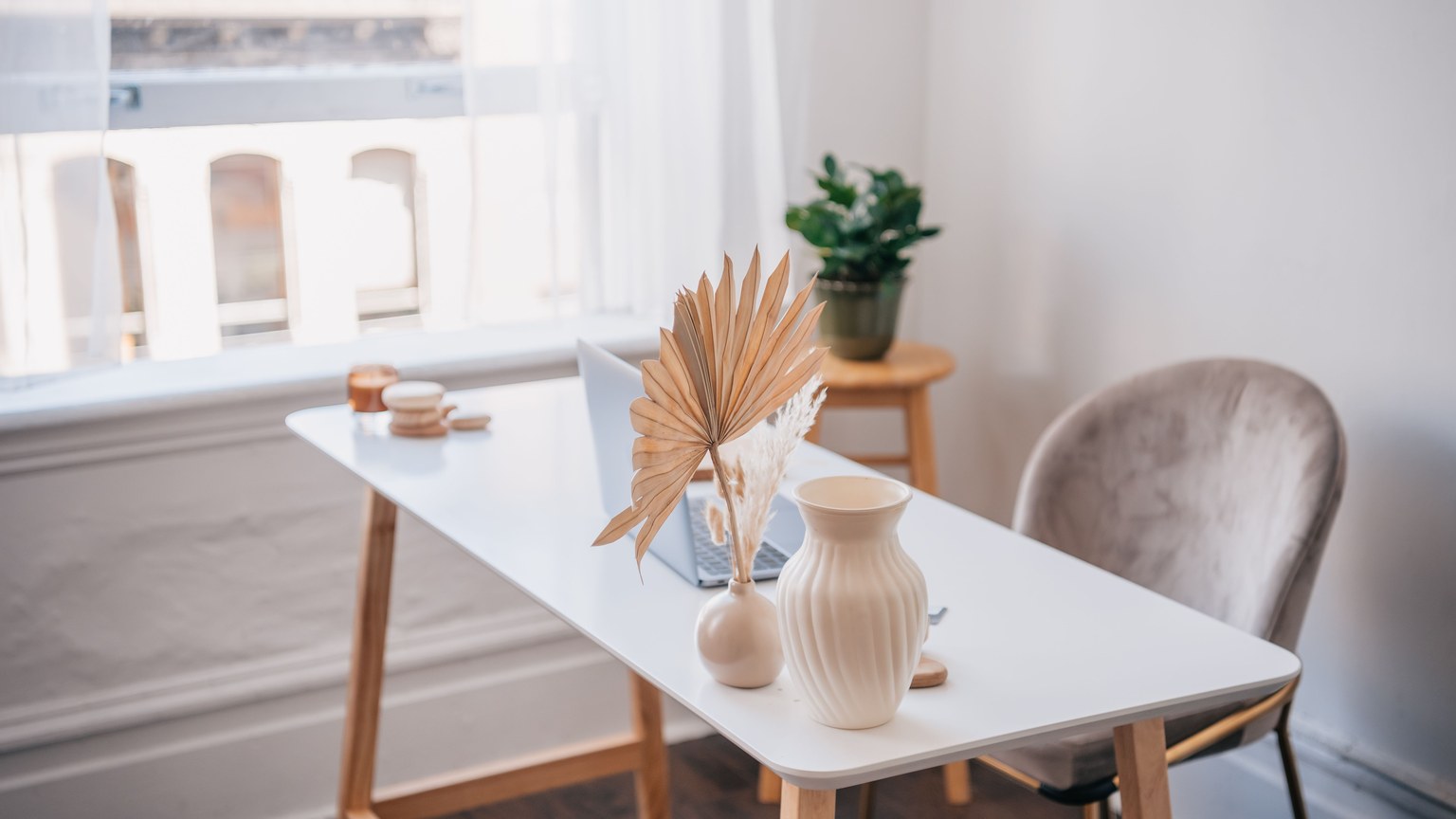 Modern office desk with laptop and minimalist decor near a window.