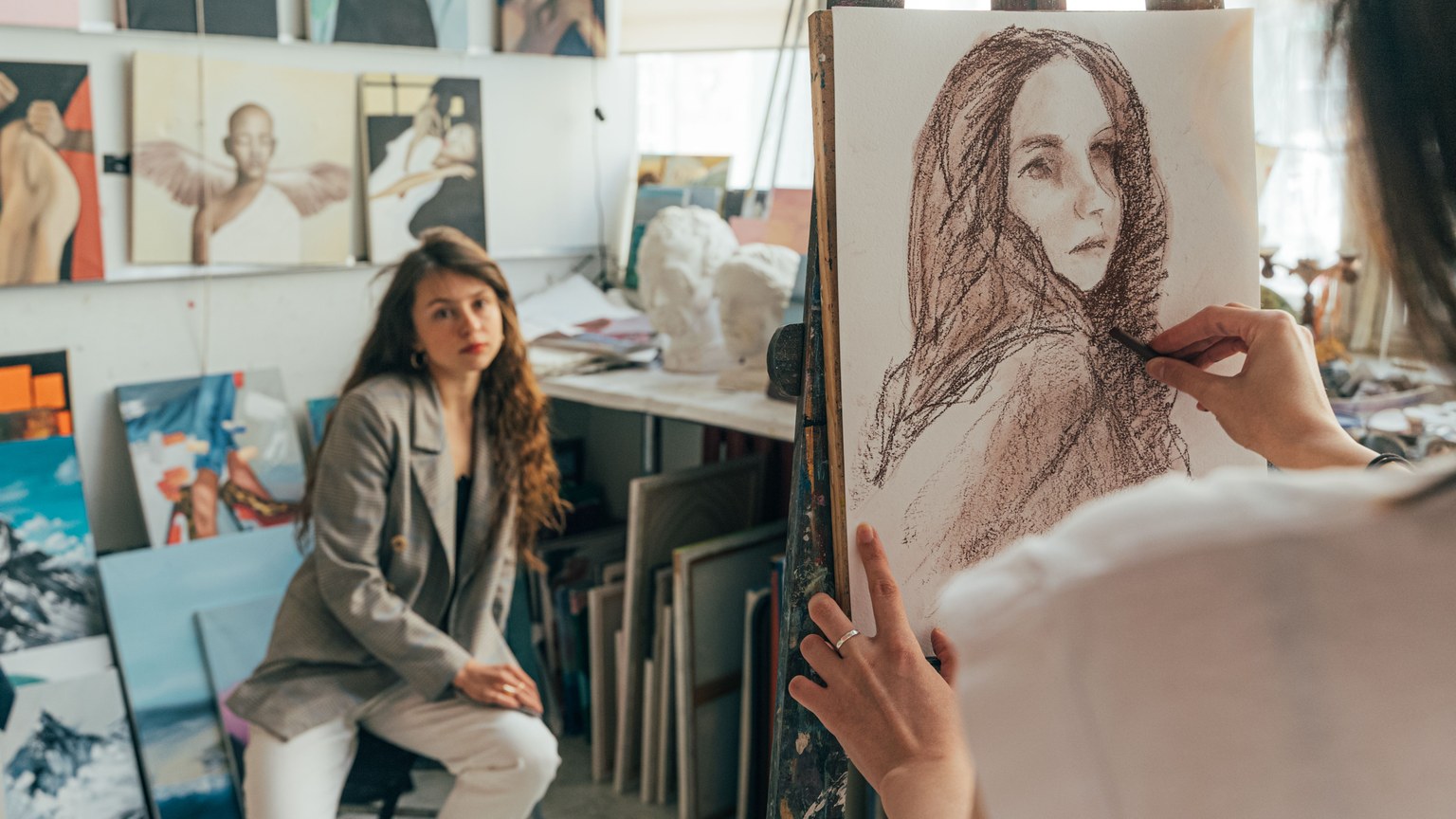 Artist sketching a portrait in a vibrant studio setting with model posing.