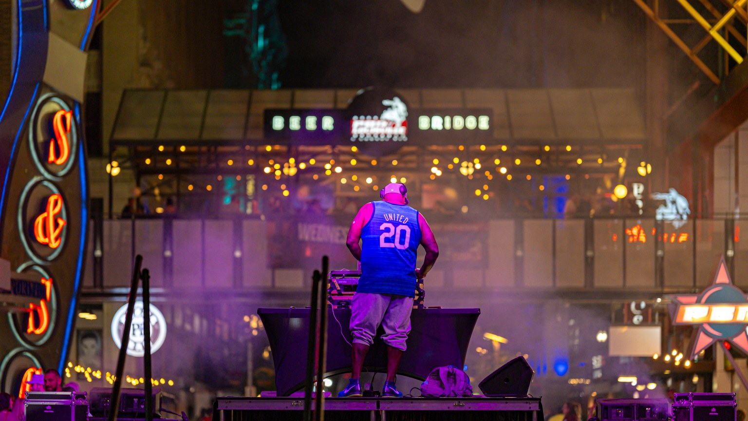 DJ performs amidst colorful lights at lively night street venue.