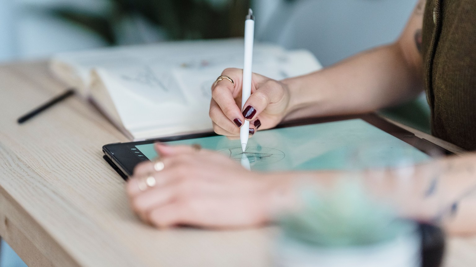 Crop unrecognizable female designer using tablet and stylus for drawing sketches on wooden table