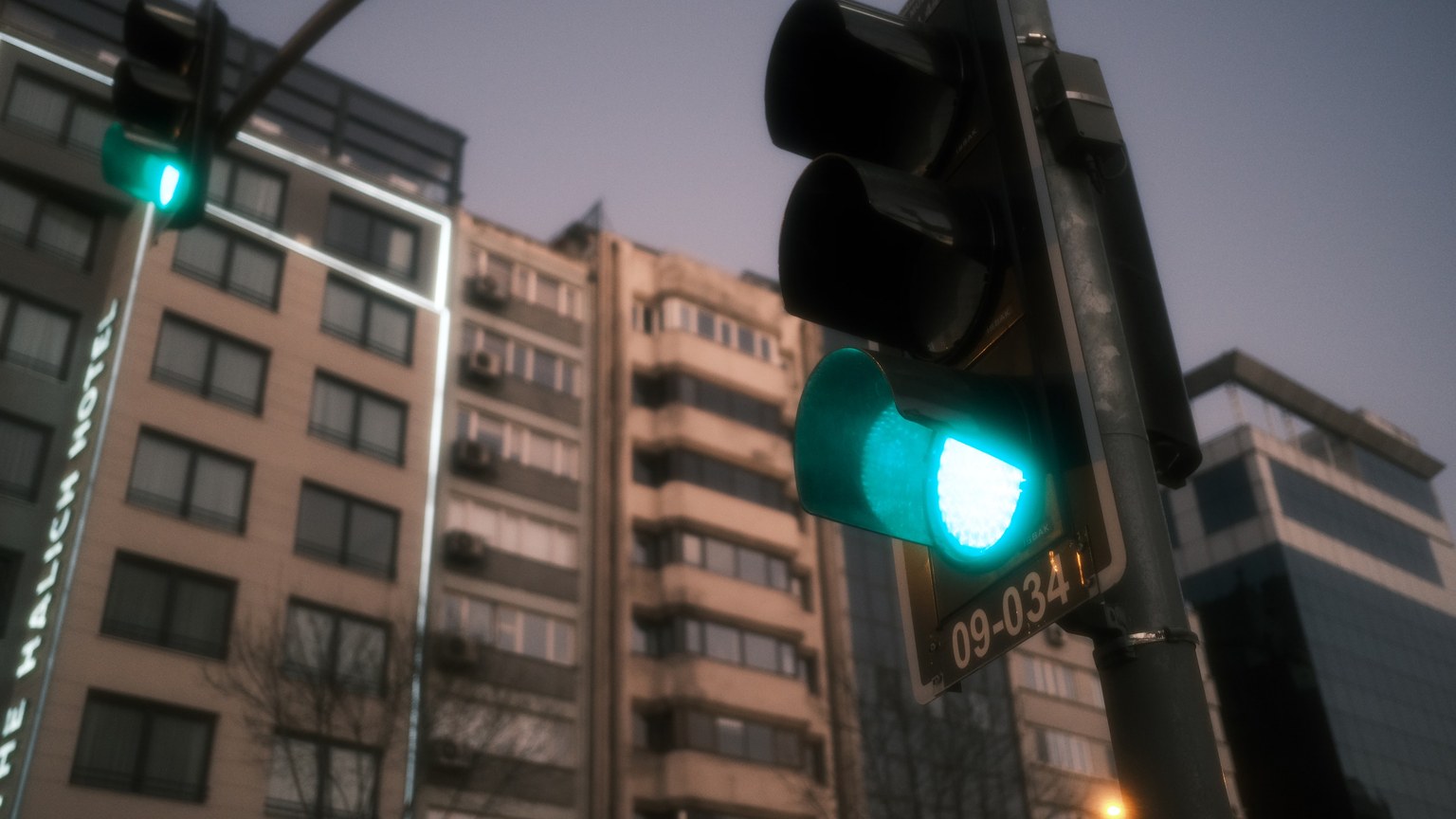 Low-angle view of a green traffic light with urban buildings in a city setting during twilight.