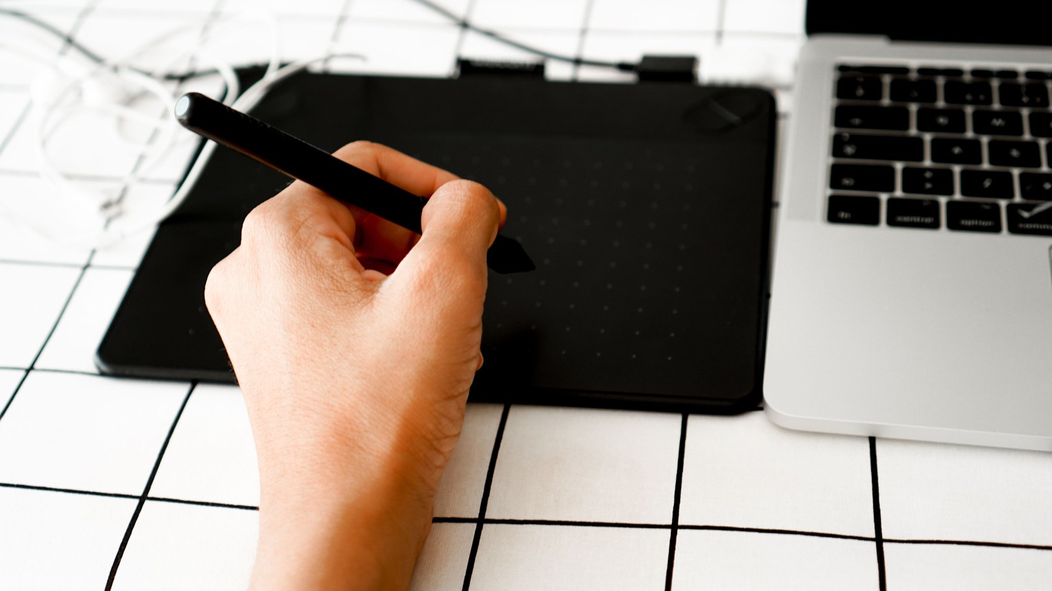Close-up of a hand using a pen tablet next to a laptop, ideal for digital design projects.