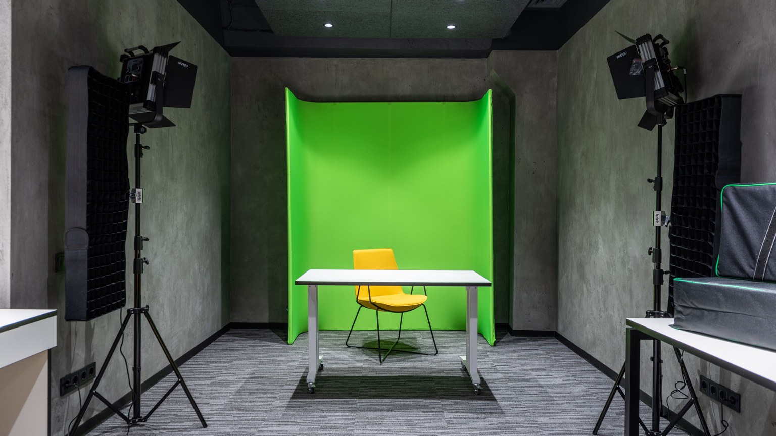 Comfortable yellow chair at white table placed near green wall in spacious modern studio with contemporary lighting equipment and professional supply