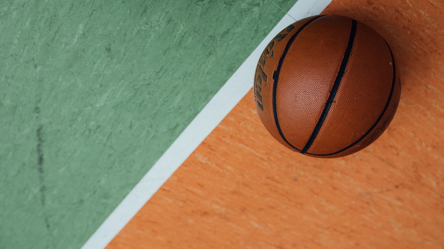 A close-up of a basketball resting on a colorful court with orange and green sections.