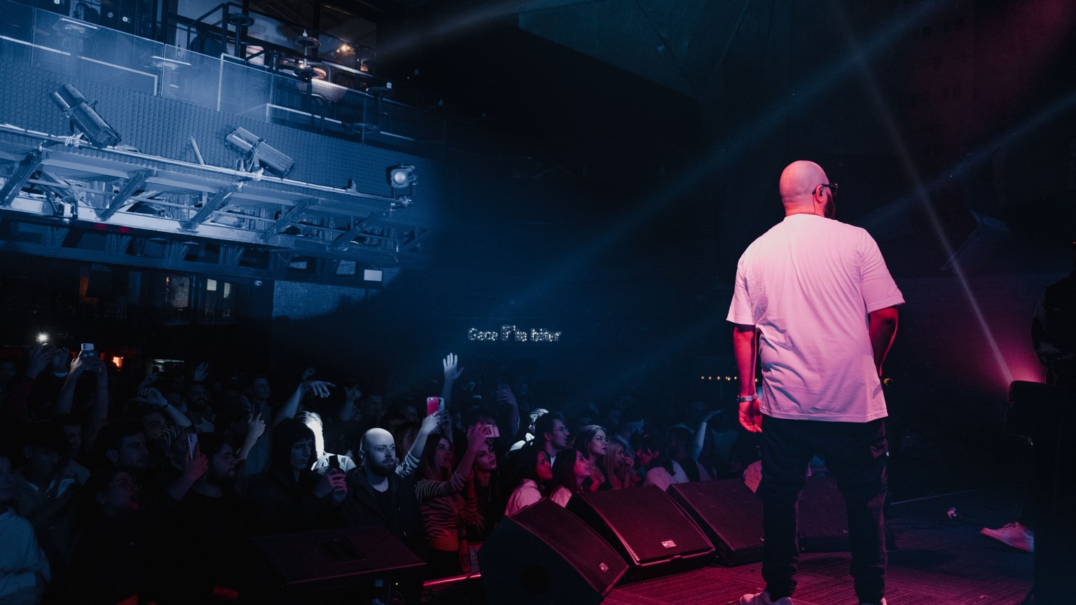 Rapper performing live on stage with vibrant lighting and engaged audience in a concert setting.