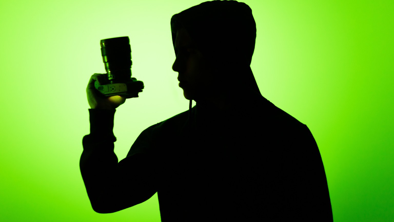 Silhouette of a person holding a camera against a vibrant green background, creating a dramatic effect.