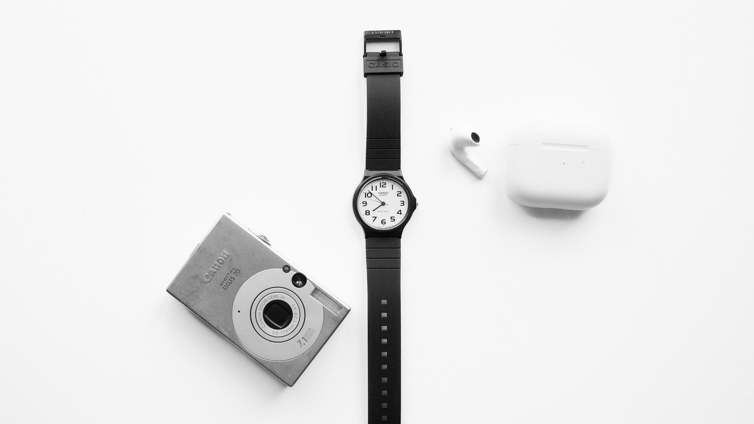 Black watch, camera, and earbuds arranged on a white background for a modern minimalist style.