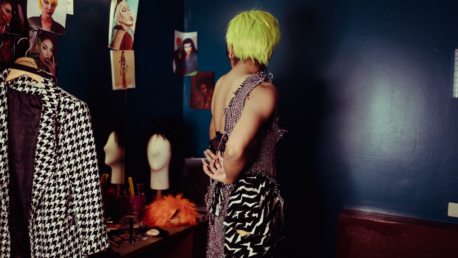 Side view unrecognizable provocative female with dyed green hair wearing strange torn dress against mirror in dark dressing room