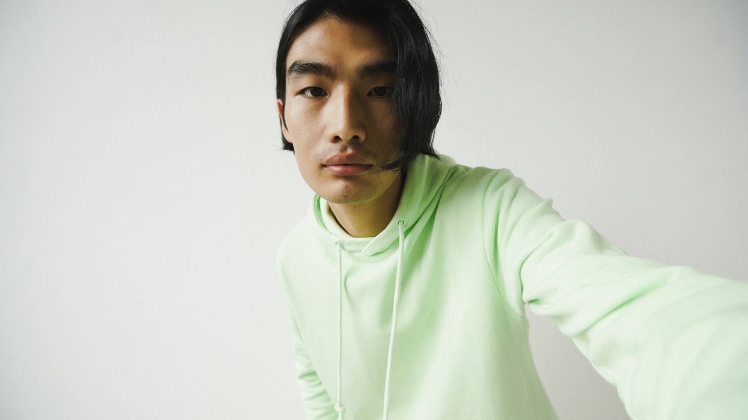 Portrait of an Asian man in a green hoodie, studio shot with a white background.