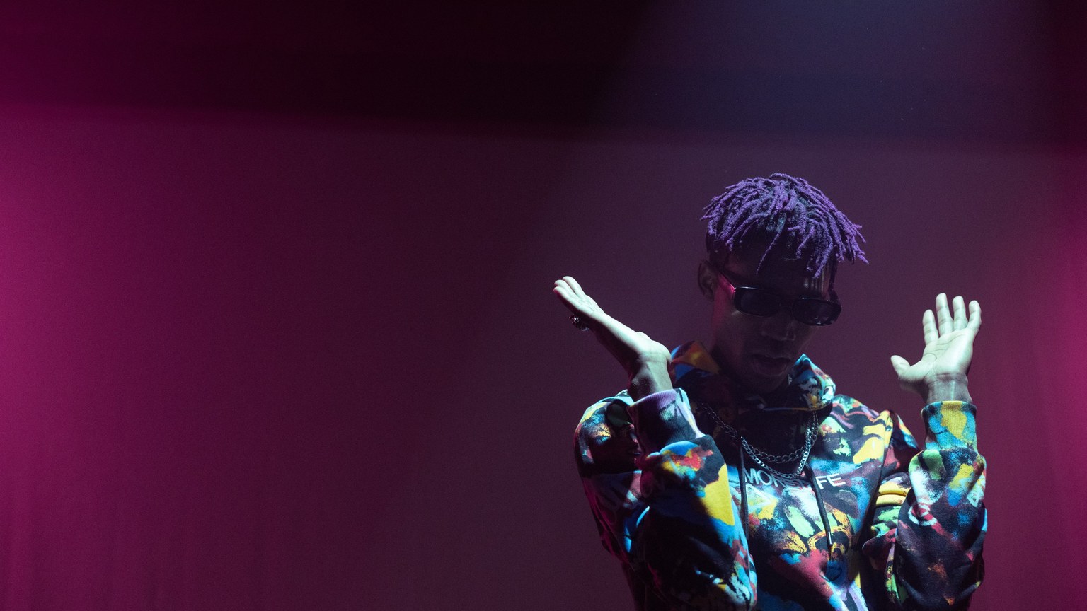 Vibrant image of a rapper performing on stage with colorful fashion and lighting.