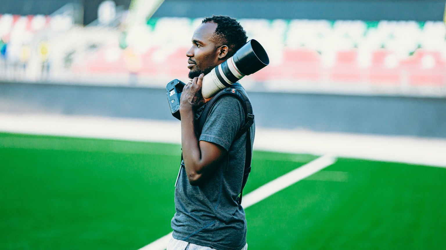 A photographer with a long lens camera stands on a sports field, capturing the action.