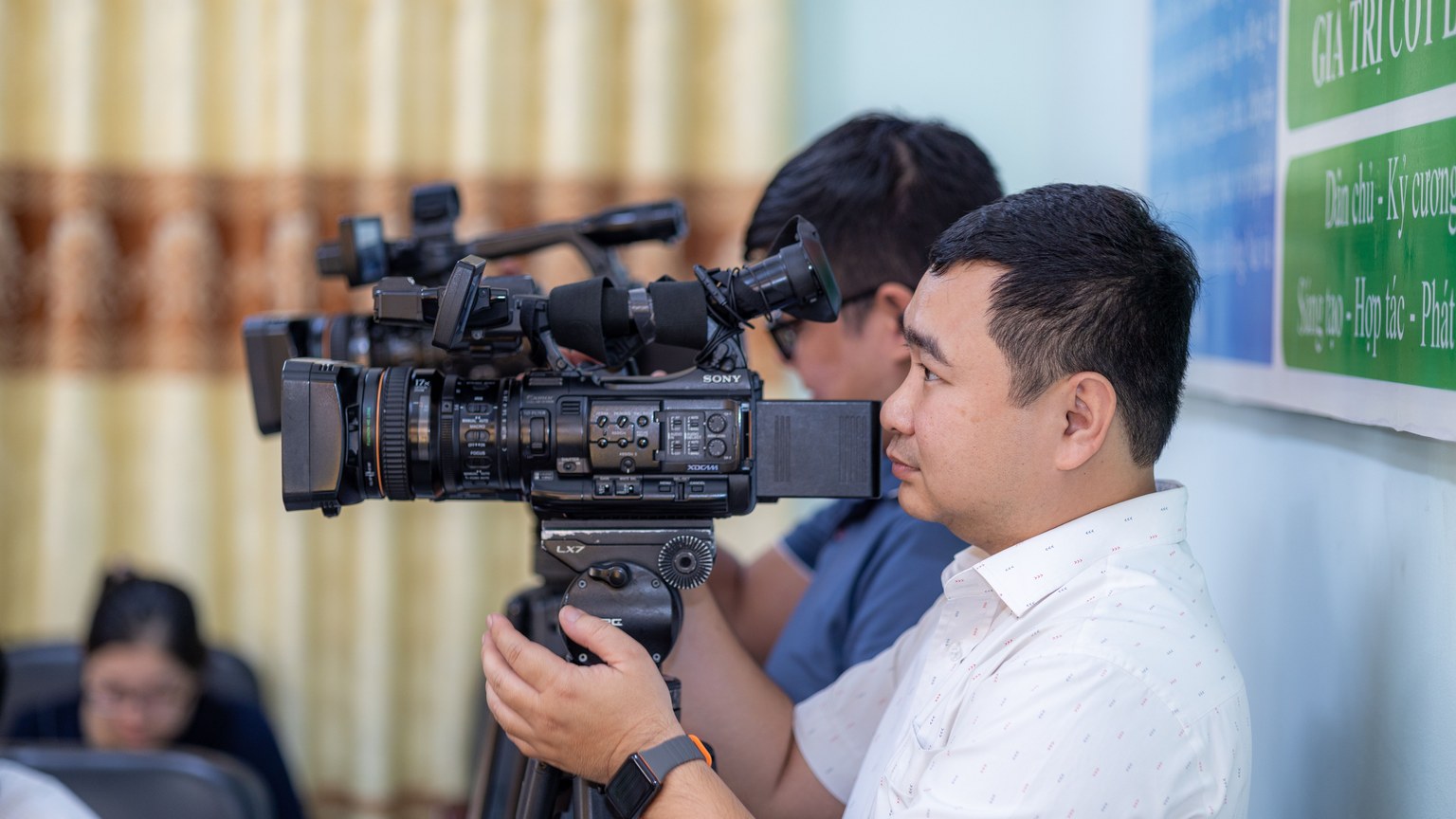 Male cameraman operating a professional video camera during an indoor event.