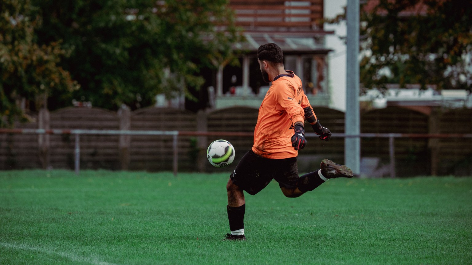 Soccer player in orange jersey kicking a ball on a lush green field during a daytime game.