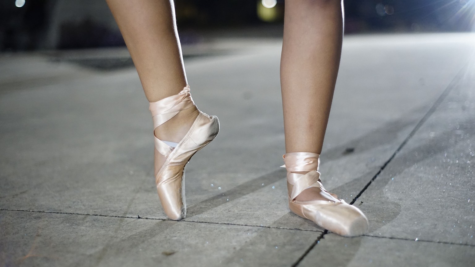 Close-up of ballet dancer's feet in pointe shoes on a nighttime concrete stage.