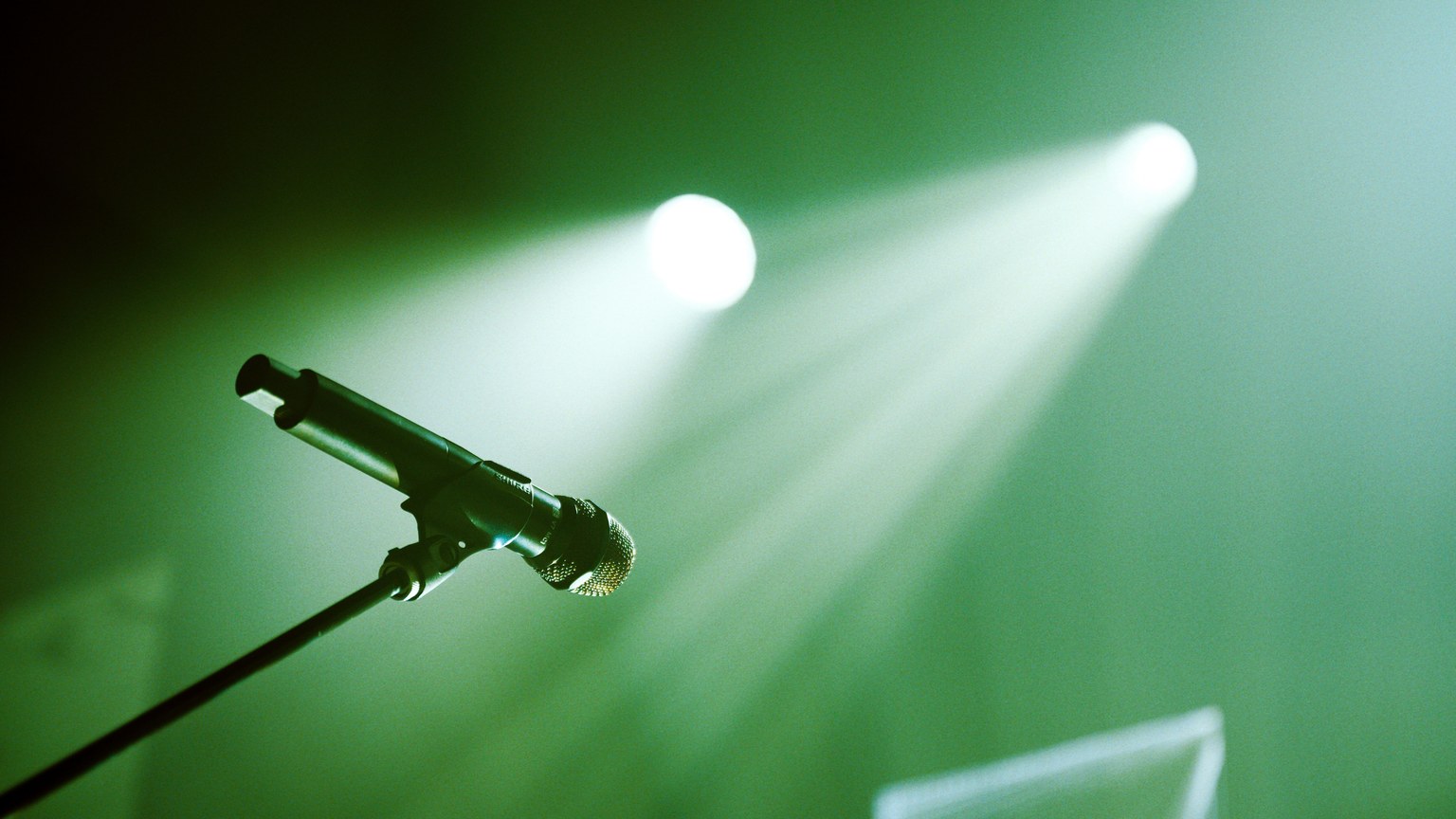 From below of black stand with microphone placed on stage with green illumination