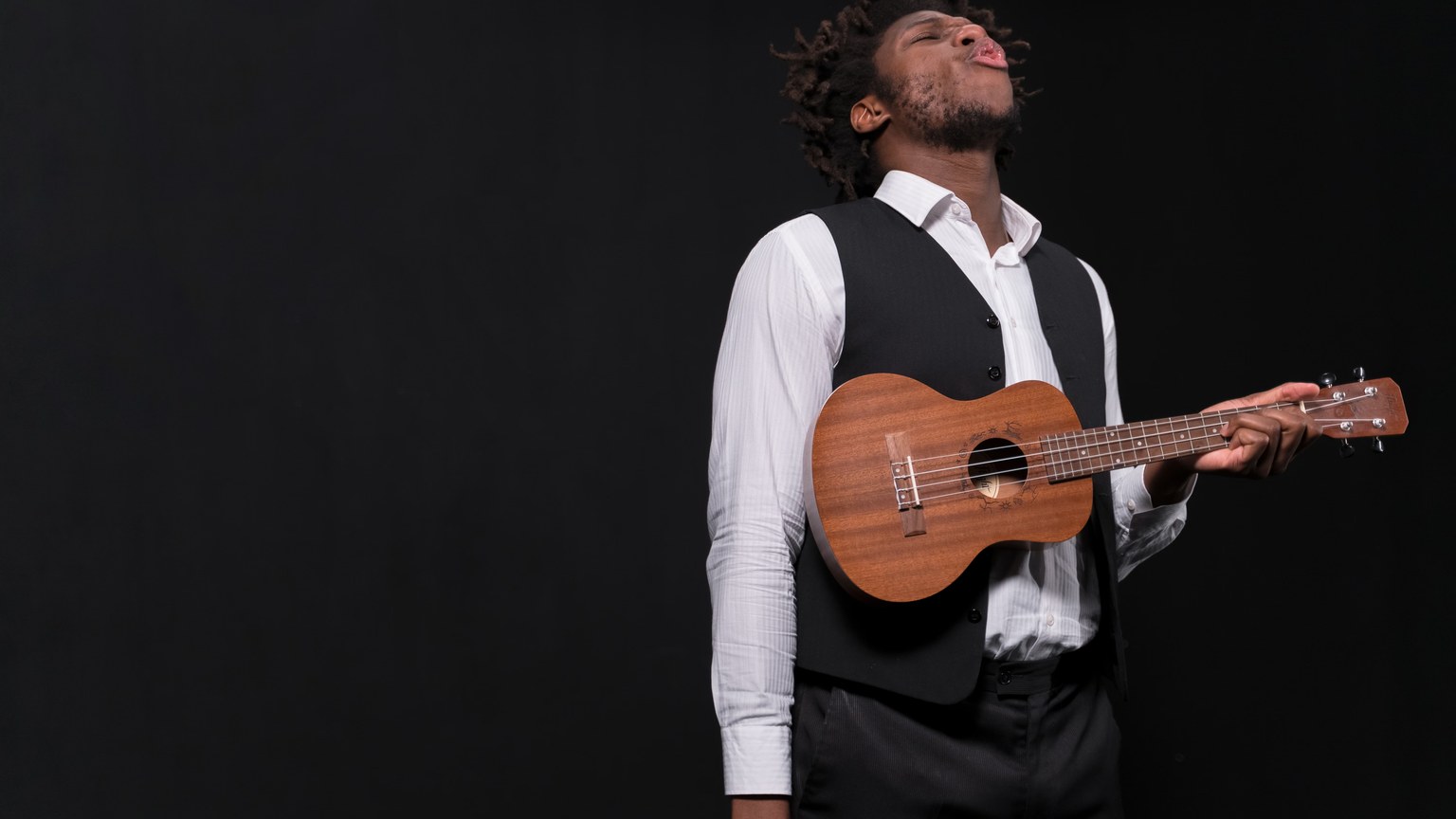 A passionate musician playing ukulele against a black backdrop, conveying emotion and artistry.
