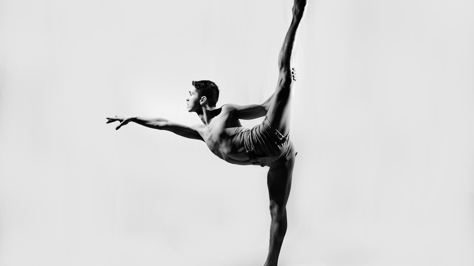 Dynamic black and white photo of a male dancer performing a perfect high kick pose.