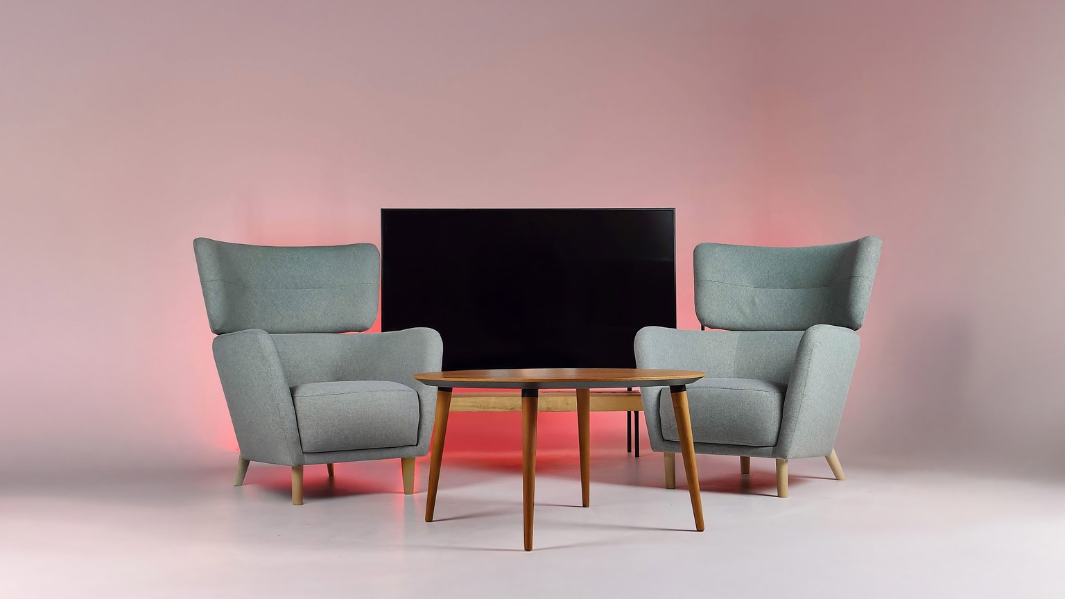 Cozy podcast studio with armchairs, table, and TV backlit in pink light.