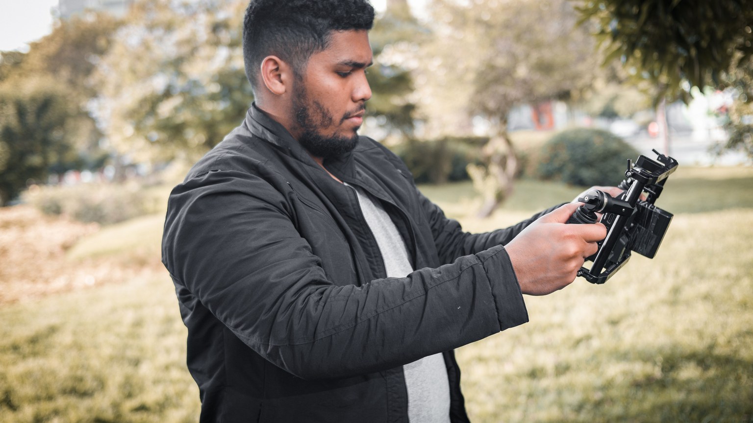 A man holding a camera rig, filming in an outdoor park setting in Lima, Peru.