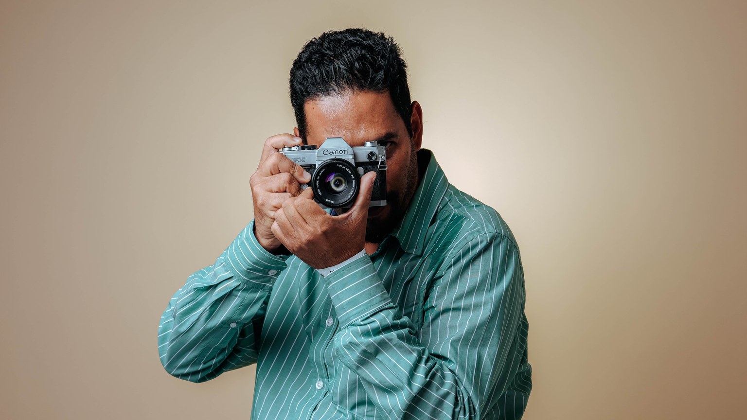 Man posing with a vintage camera in a studio setting wearing a striped green shirt.
