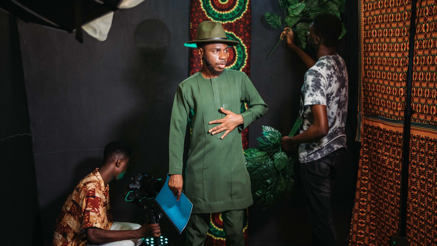 A backstage look at a fashion photoshoot with men in traditional green attire, creating a vibrant setup.