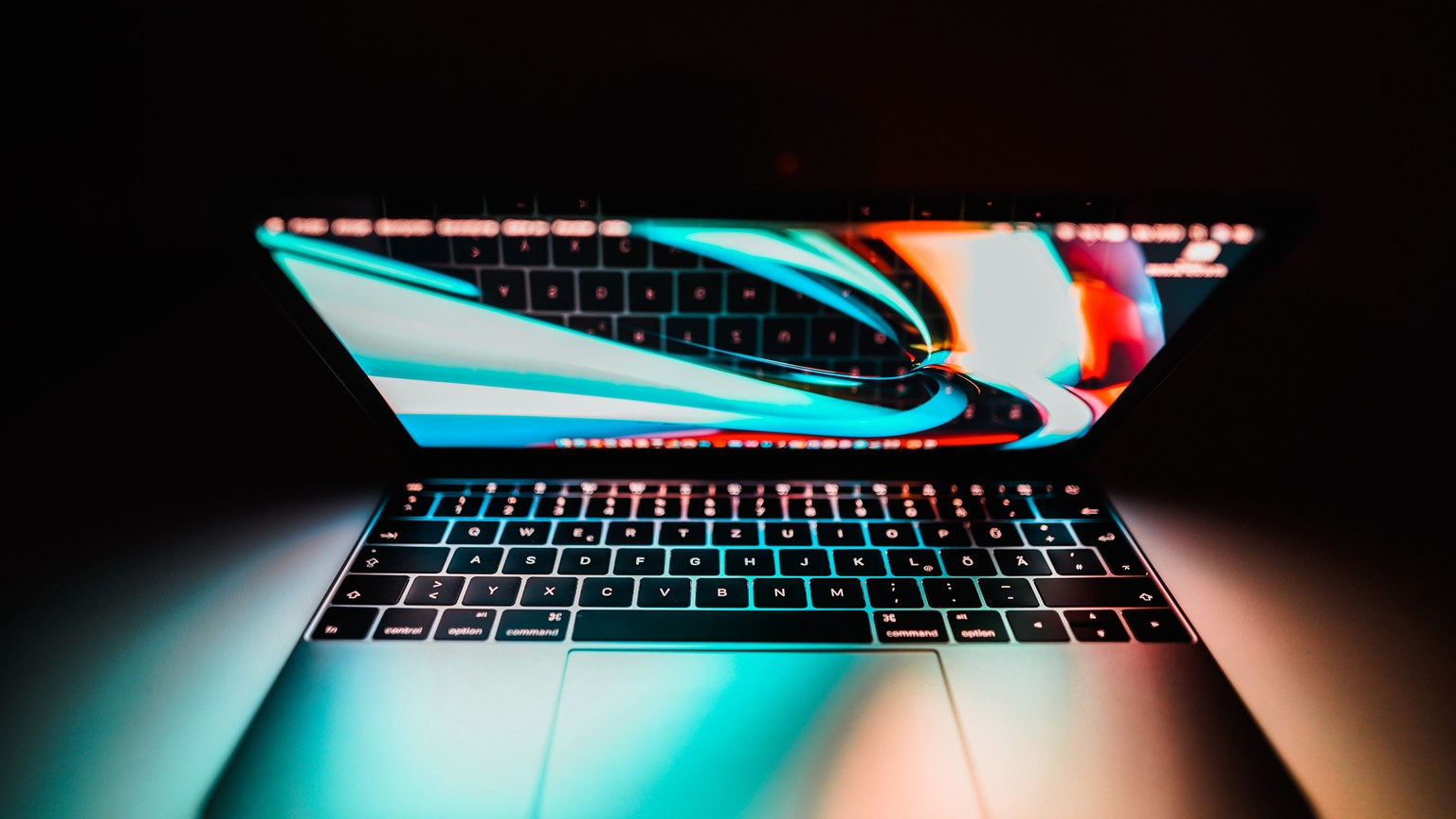 Open laptop with a colorful display reflecting on its keyboard, set against a dark background.