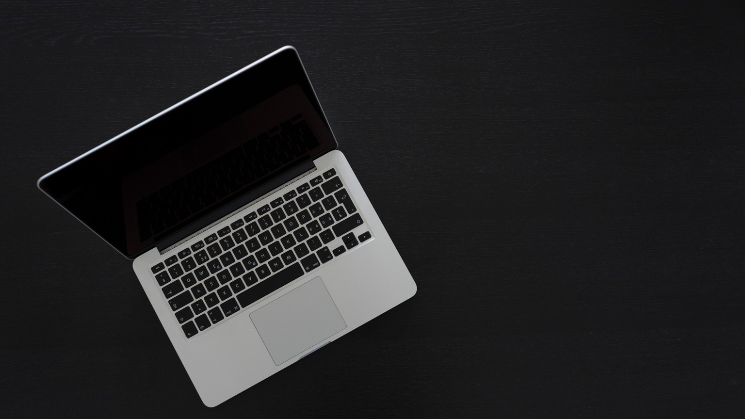 Overhead view of a MacBook laptop on a dark desk, showcasing modern technology and minimalism.