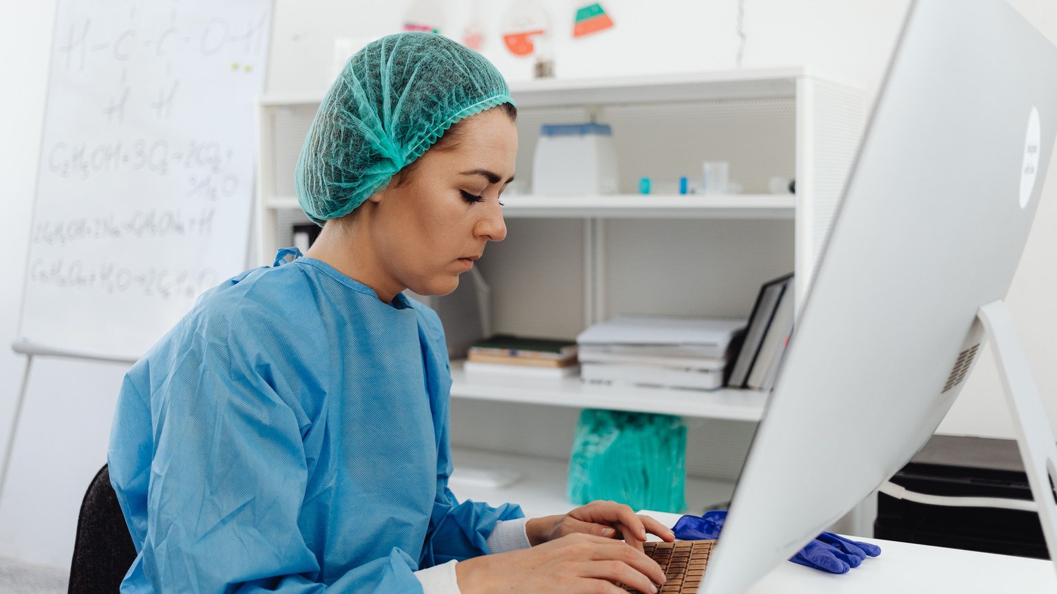 A female healthcare professional in scrub suit working on a computer in a laboratory setting.