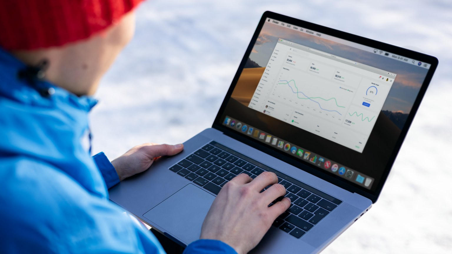 Person working on a laptop analyzing charts in an outdoor setting during winter.