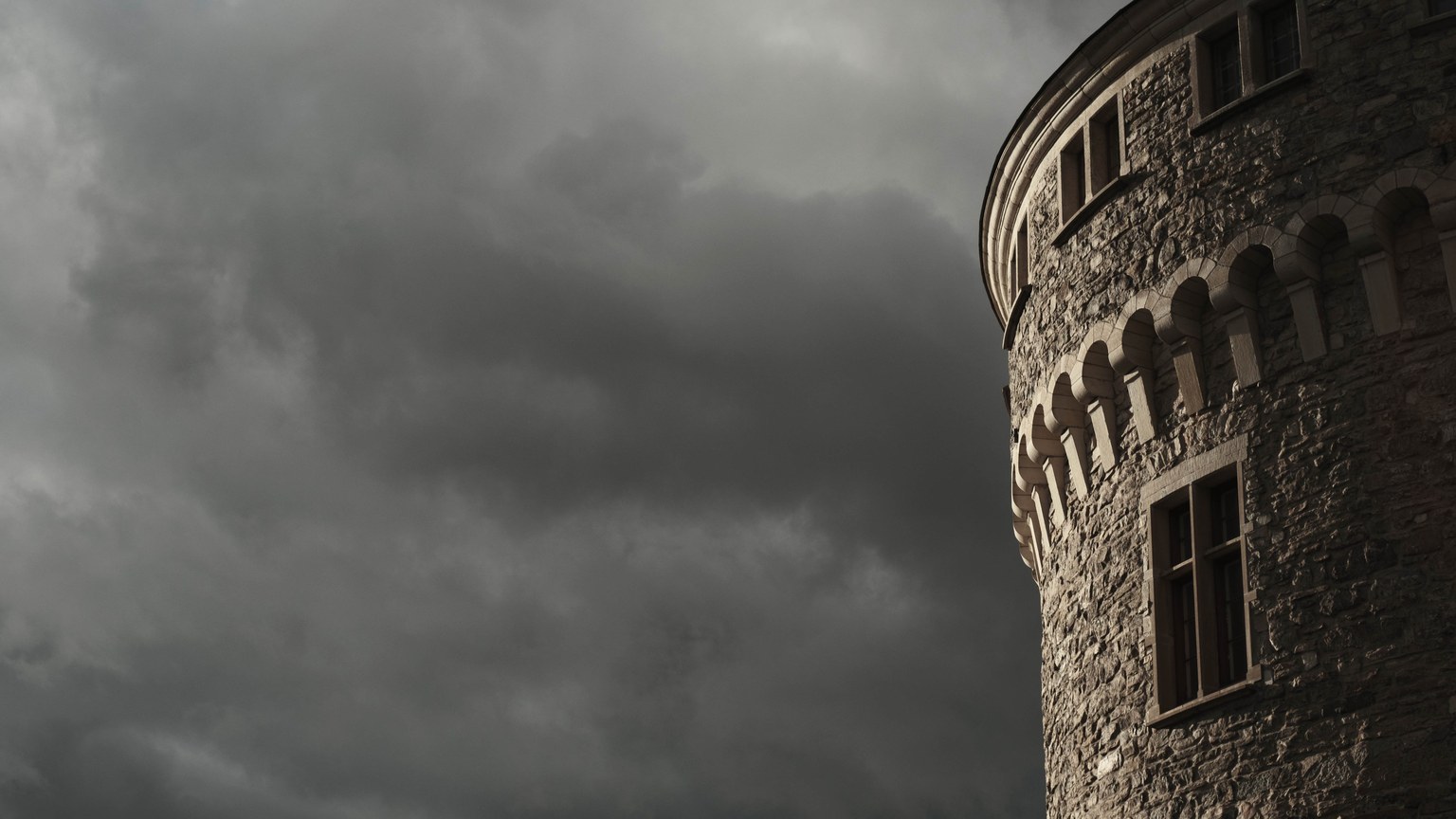 A historic stone tower rises against a dramatic, moody sky with dark clouds.