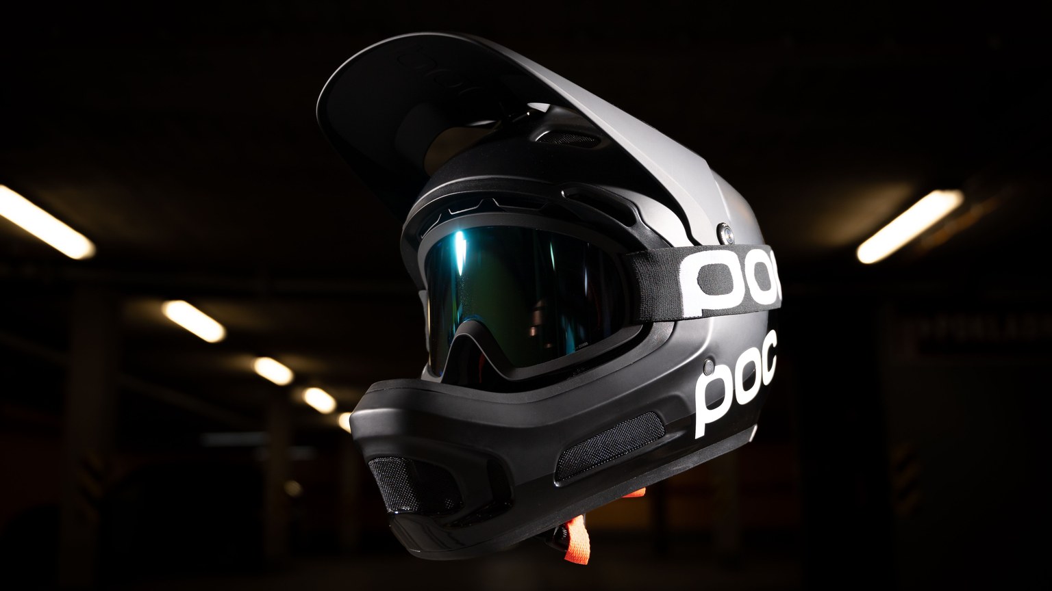 Black racing helmet with goggles, illuminated in a dark setting, showcasing modern design and safety features.
